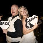 A man and woman holding bride and groom signs.